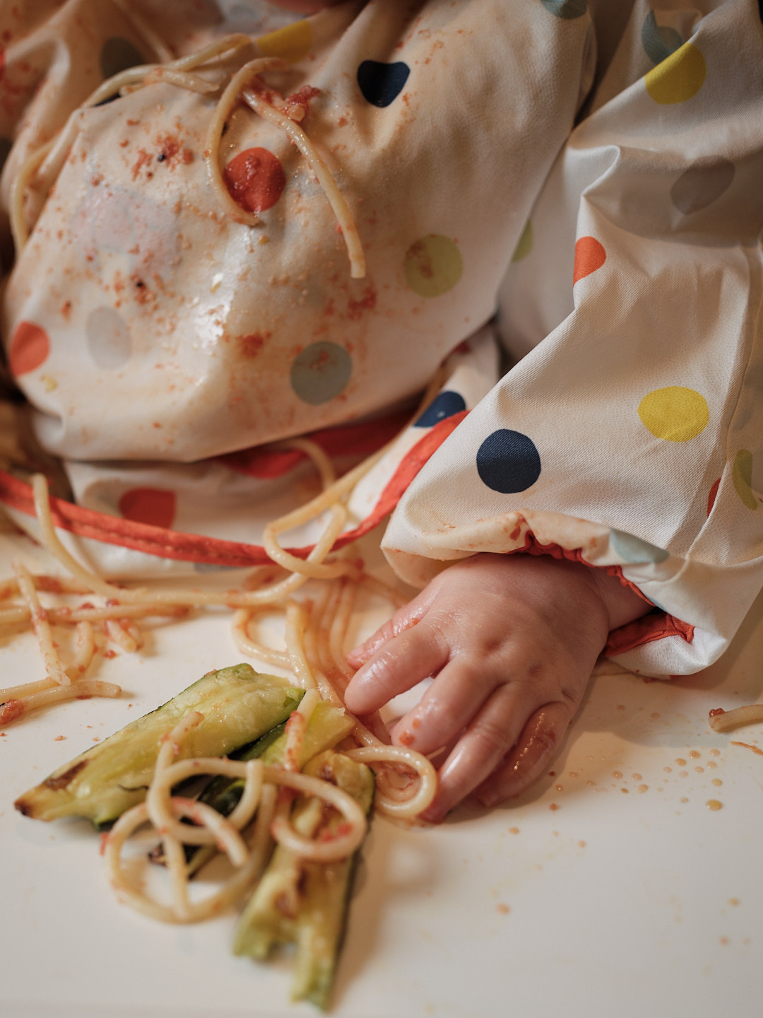 A baby's hand grabbing pasta and courgettes from a table top.