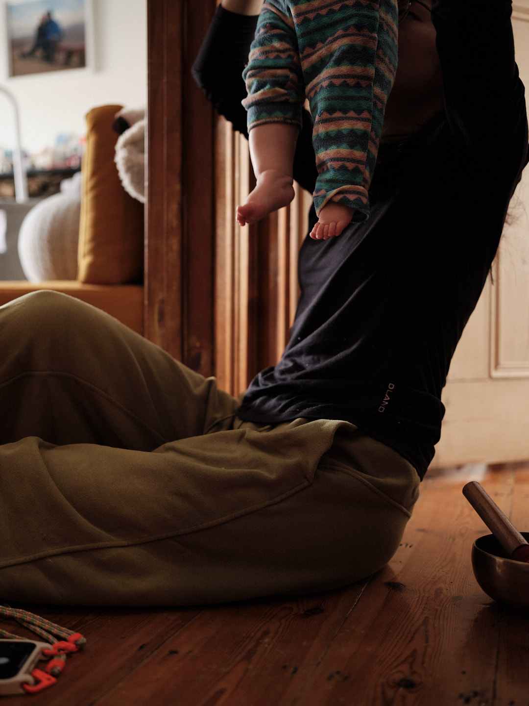 A young woman sitting on a hardwood floor lifting her daughter up to smell her butt.