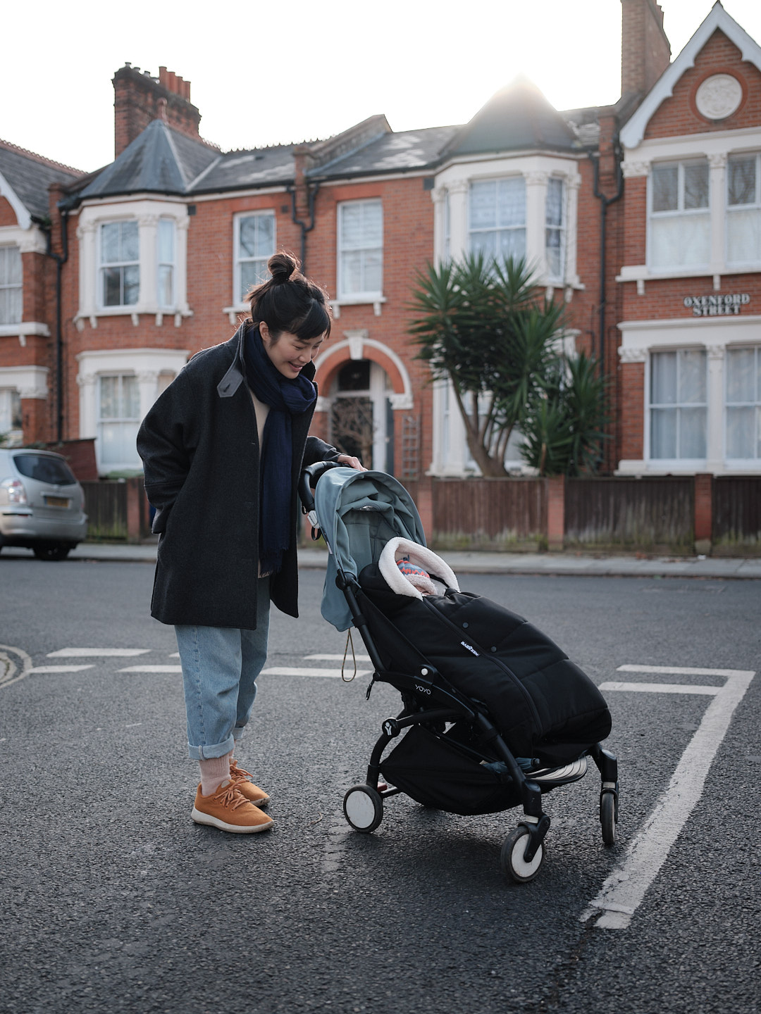 A young woman with her hand on a pram, looking down at the warmly bundled baby sitting within.