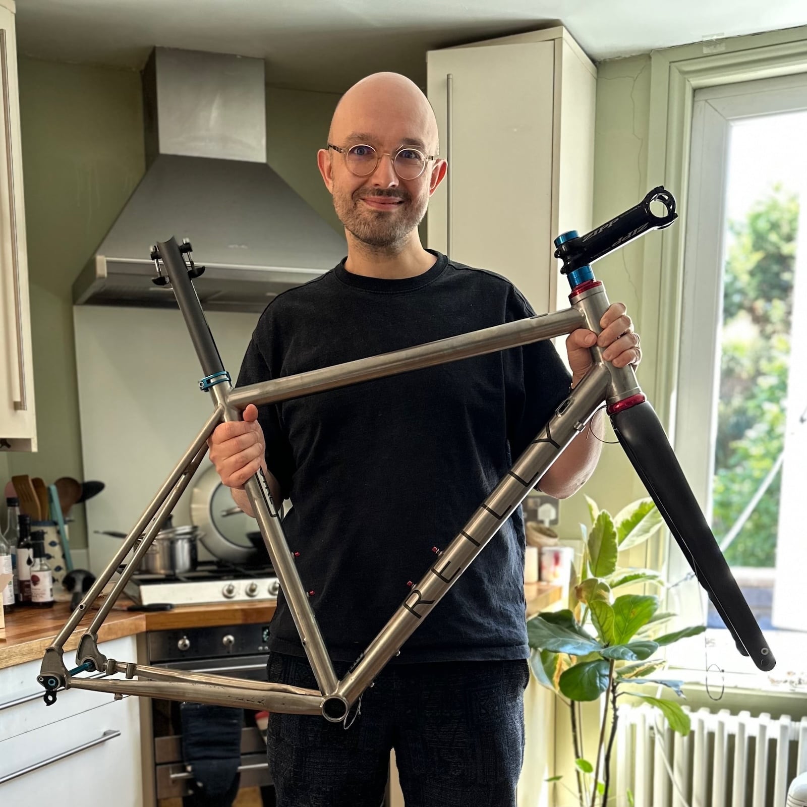 A photo of the author in his kitchen holding up a raod bike frameset and smiling