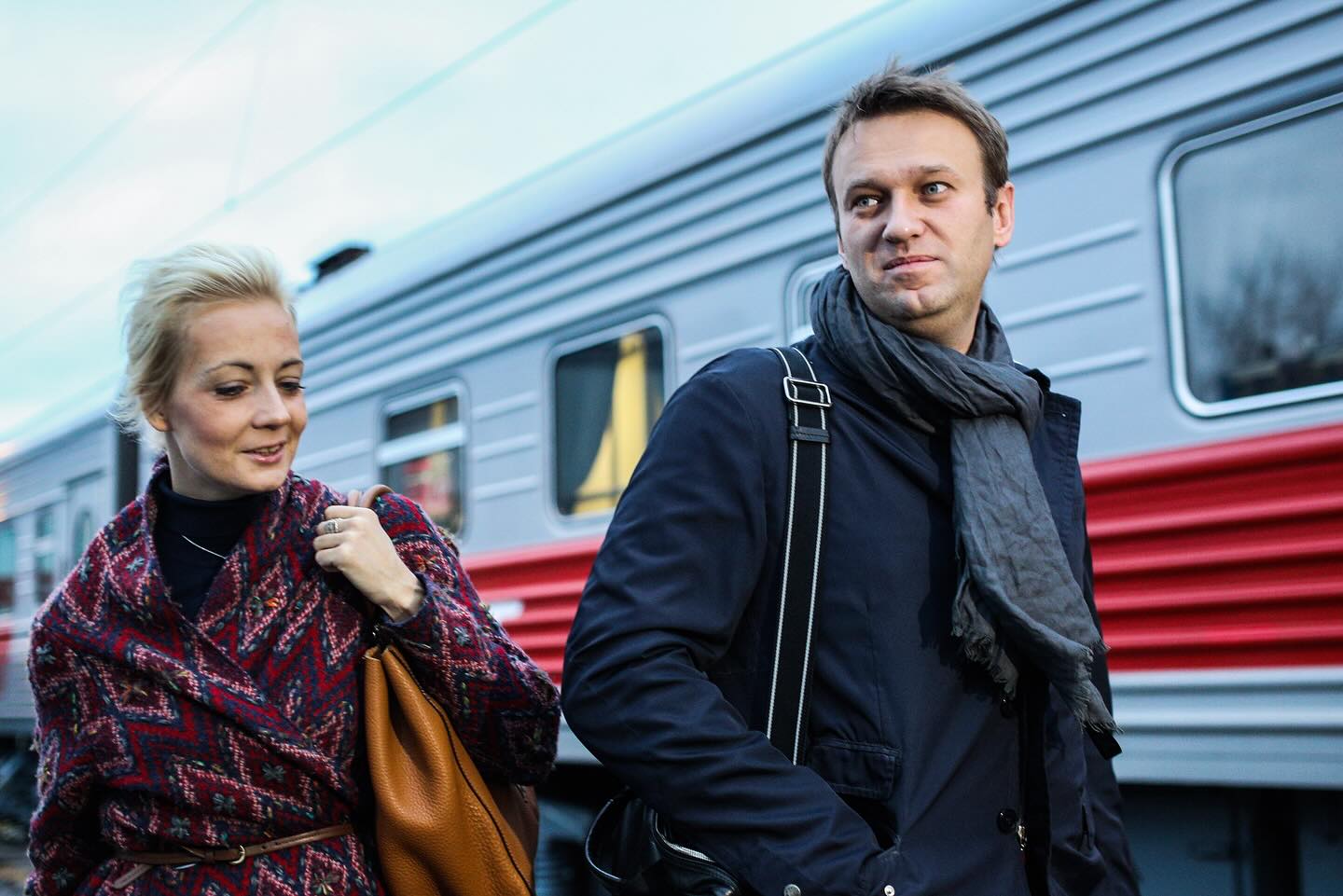 A photograph of Alexei Navalny and his wife Yulia sitting on stairs next to a campaigner holding a sign in his support.