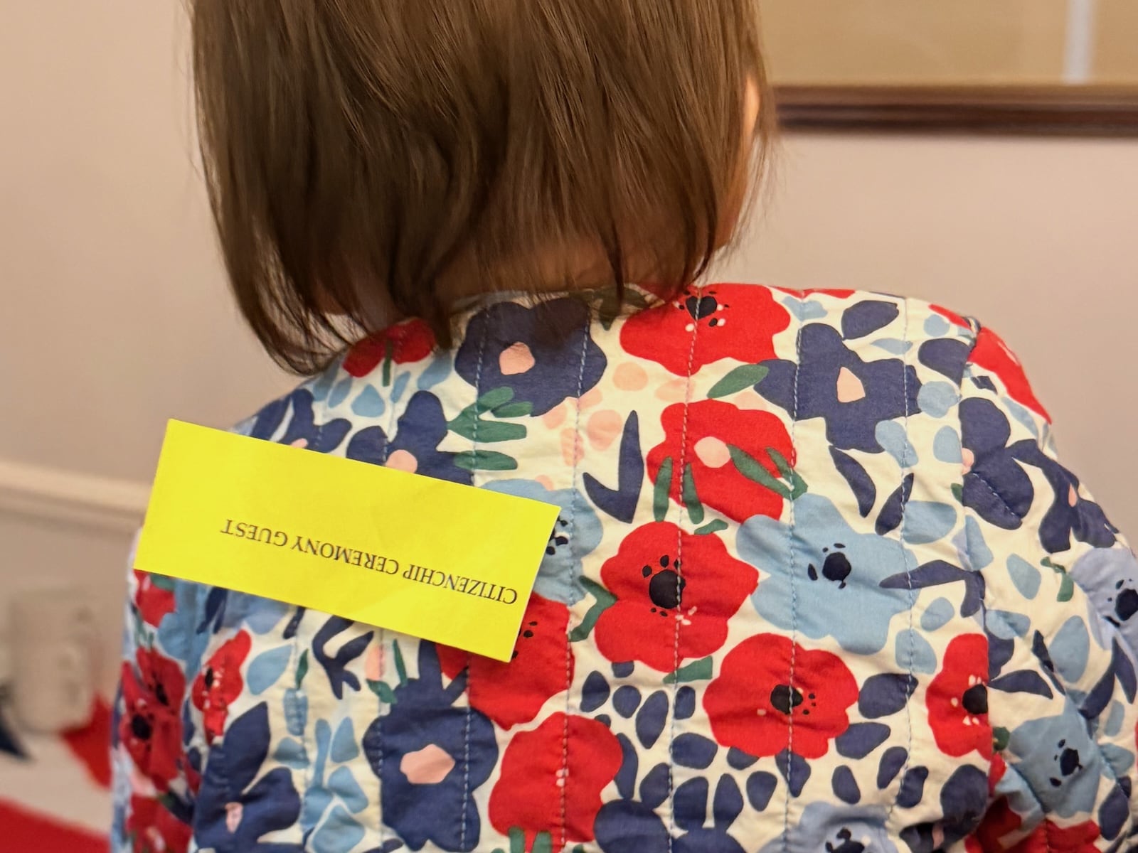 A baby with a sticker saying 'citizenship ceremony guest' on the back of his jacket