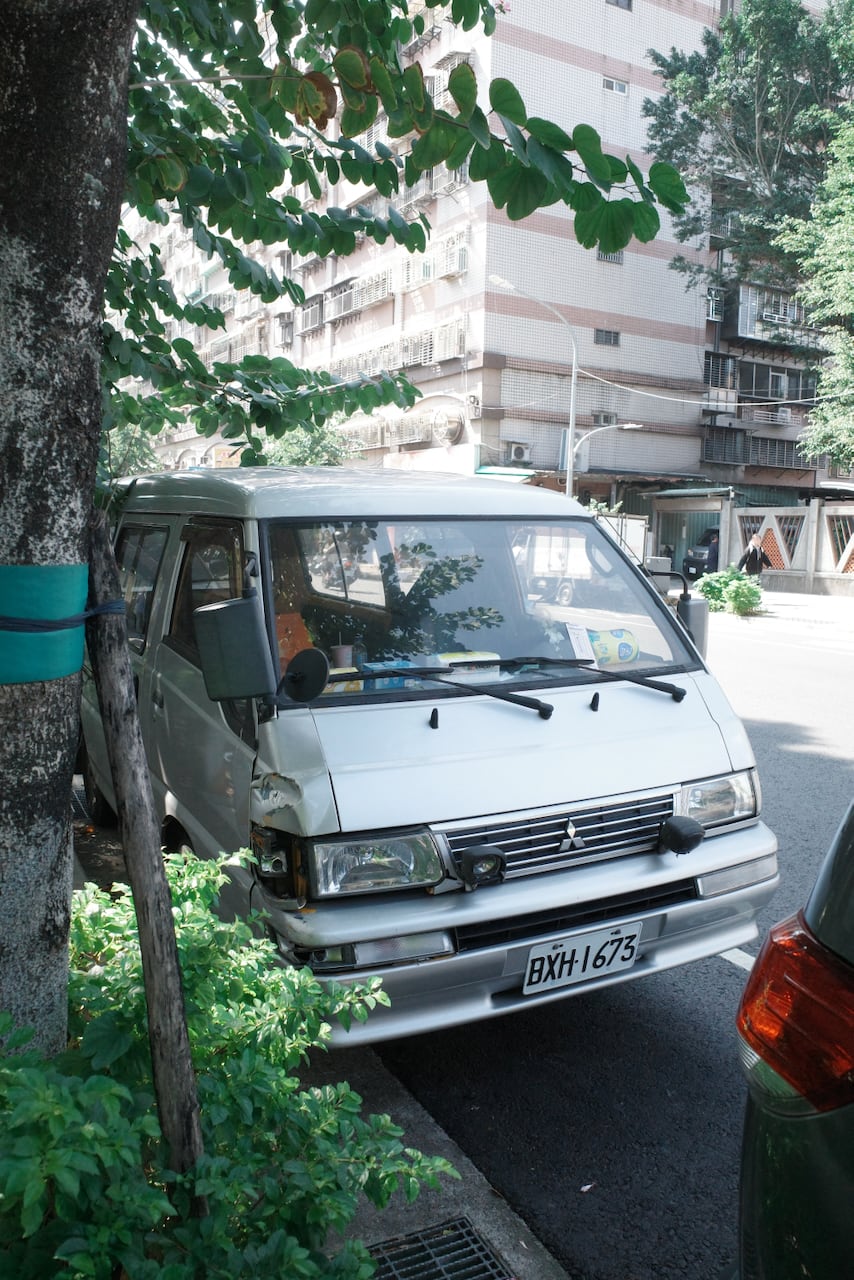 A vintage van variant in silver, with a busted passenger side turn signal parked in New Taipei City