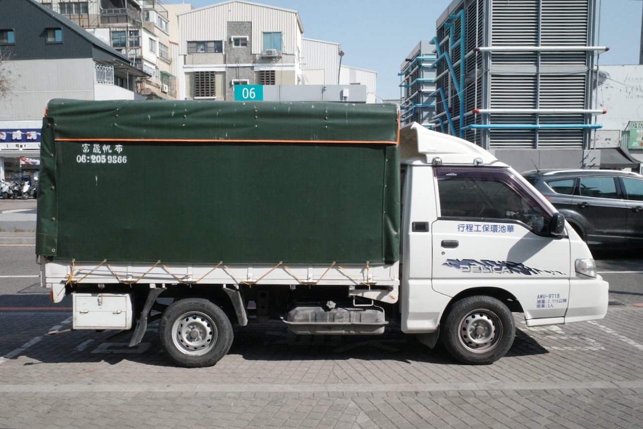 A white Delica truck with a green tarp on a parking lot in Tainan