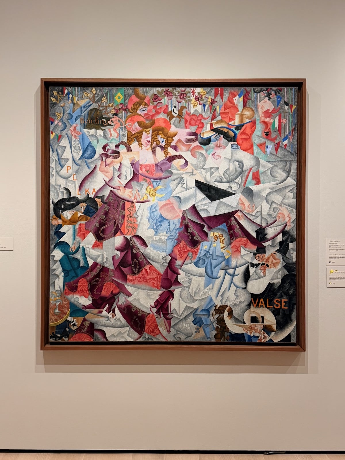 A photograph of a large, colourful futurist painting of dancers in a Paris cabaret: fragmented swirling figures in purple, red and blue dresses, with the words ‘POLKA’ and ‘VALSE’ painted in among the shapes