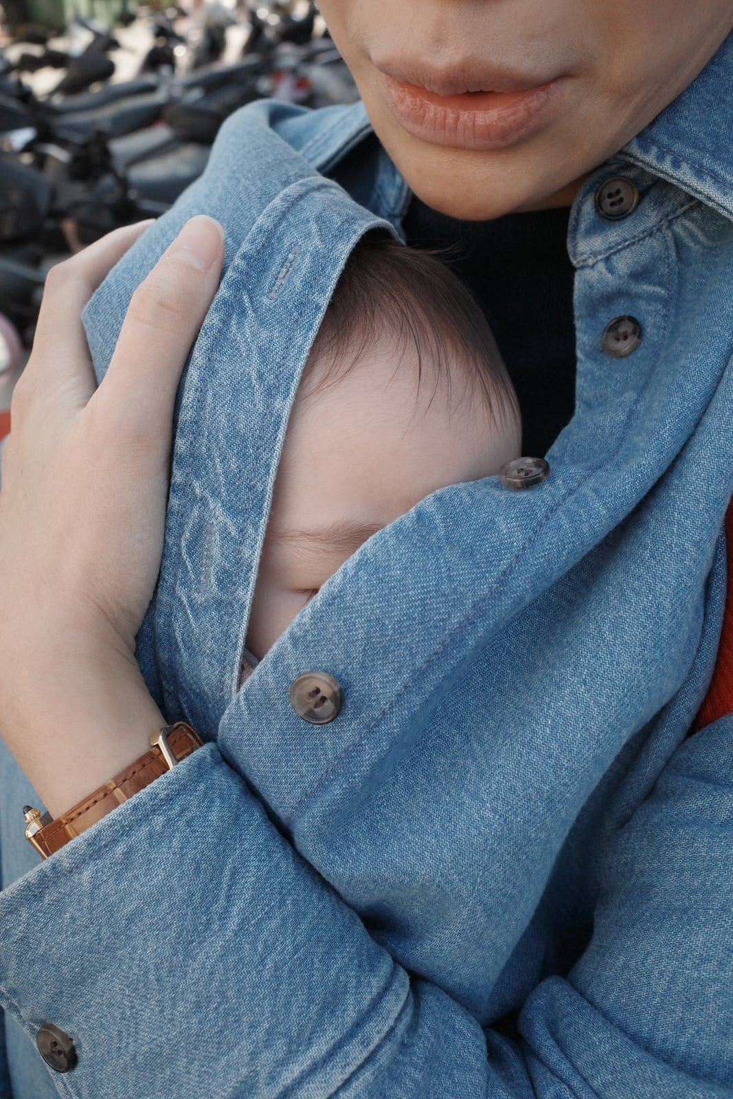 A mother and her baby wrapped under her shirt, his forehead and the hint of an eye poking out