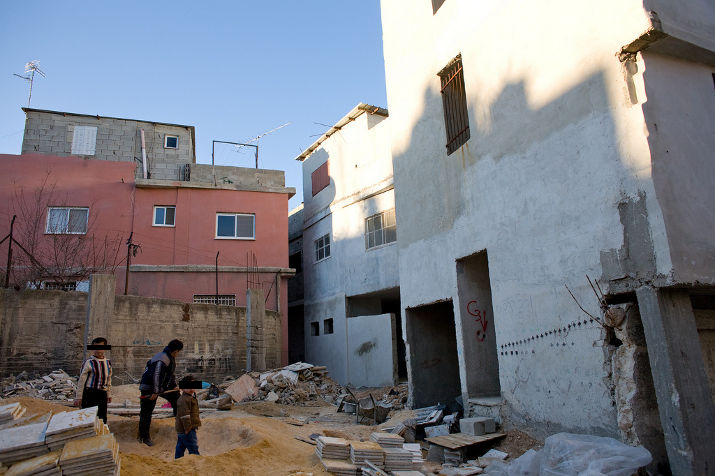 Concrete block houses around a rubble-filled lot where people sort building stones