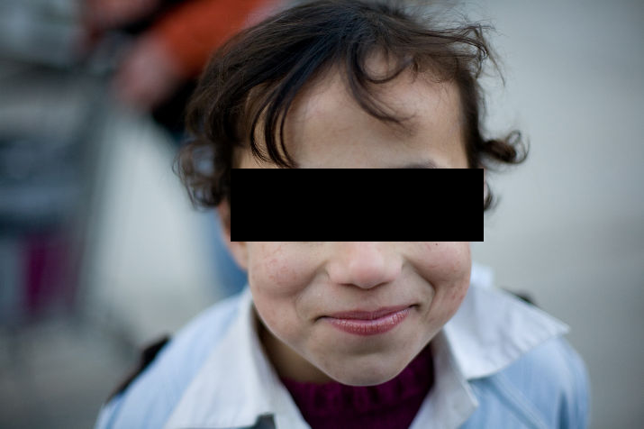 Close-up of a smiling girl with curly hair, eyes covered by a black bar