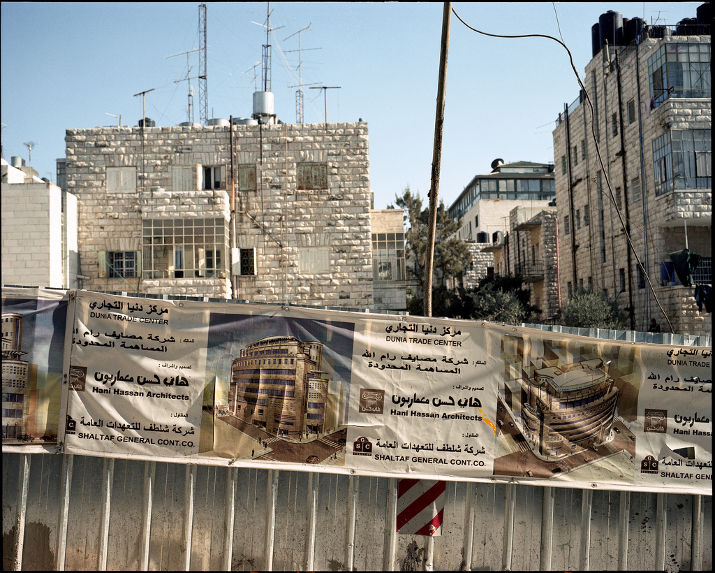 Banners for the Dunia Trade Center on a construction site fence, with stone apartment buildings and antennas behind