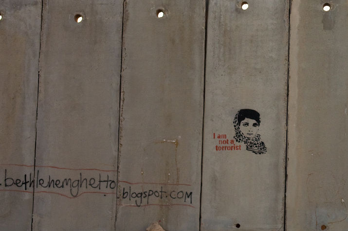 Concrete wall panels with a stencil of a woman in a keffiyeh reading I am not a terrorist, and a blog address painted below
