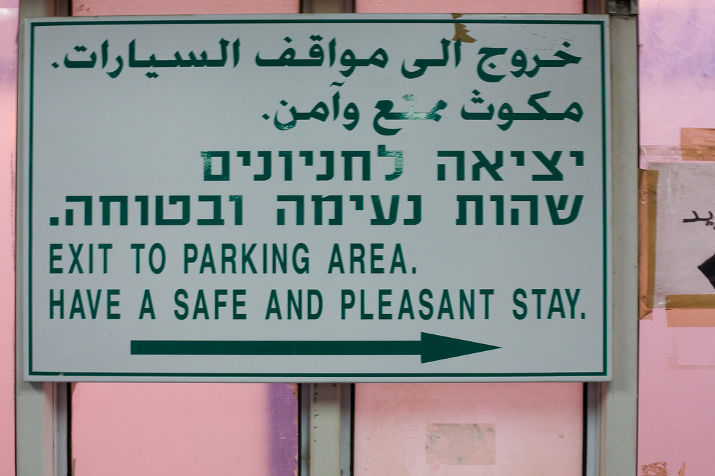 A sign in Arabic, Hebrew and English reading Exit to parking area, Have a safe and pleasant stay, with an arrow