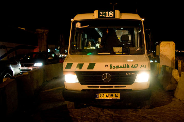 A green and white Mercedes minibus with route number 18 and Ramallah on its front, at night