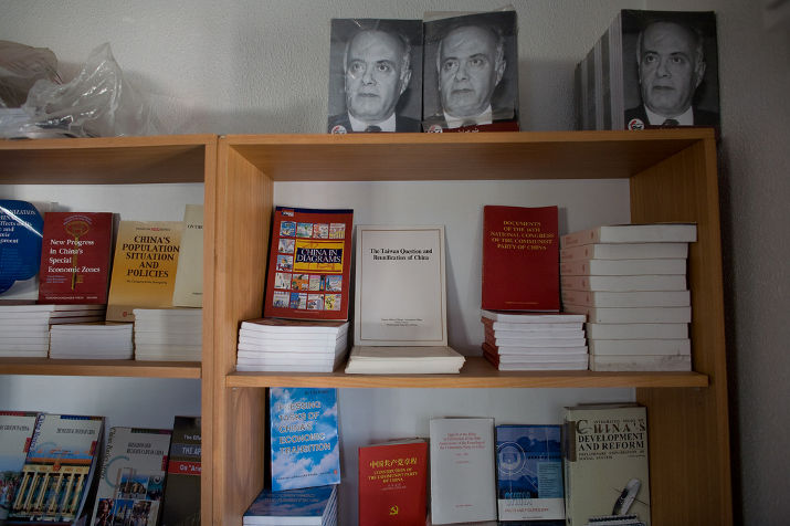 A bookcase of books about China, with three identical portraits of a man on top