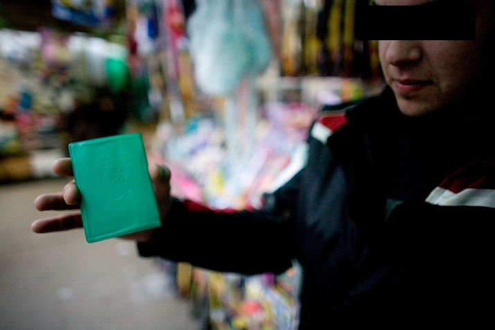 A young man, eyes covered by a black bar, holds up a green Palestinian Authority identity card
