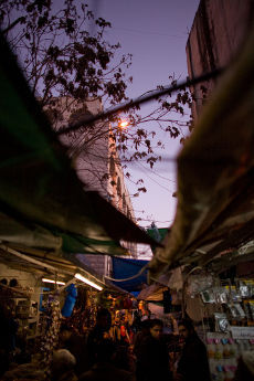 Dusk in the souk, tarpaulins and a bare tree overhead, shoppers among lit stalls below