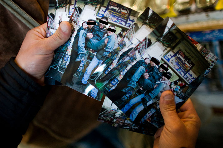 Hands holding freshly printed photographs of the young men posing in the market